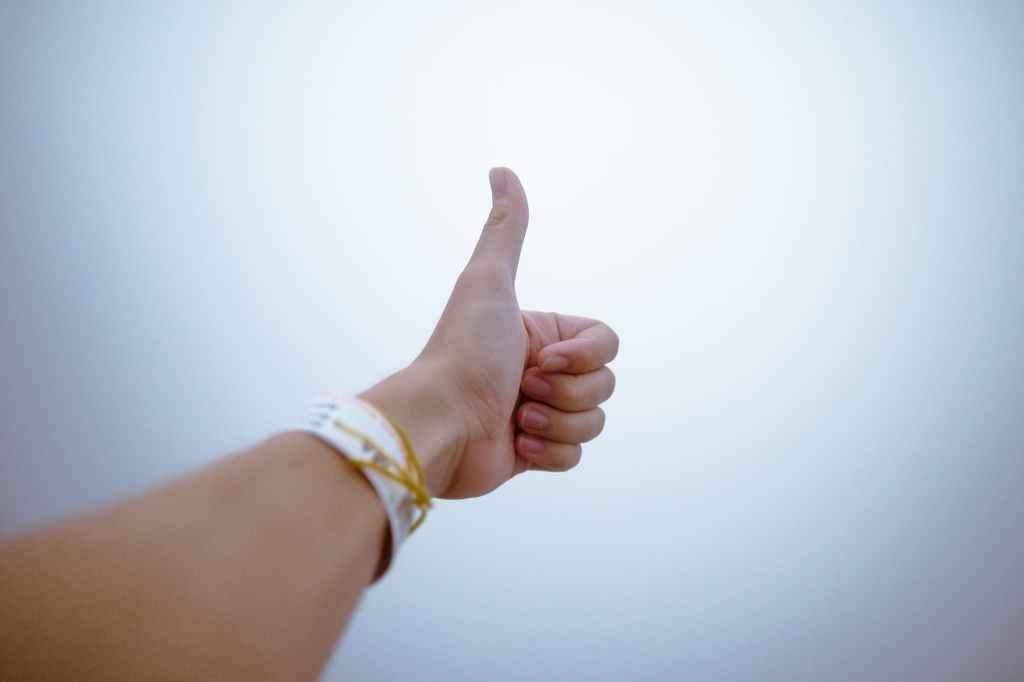 Female arm with thumb up on one hand against white glowing background